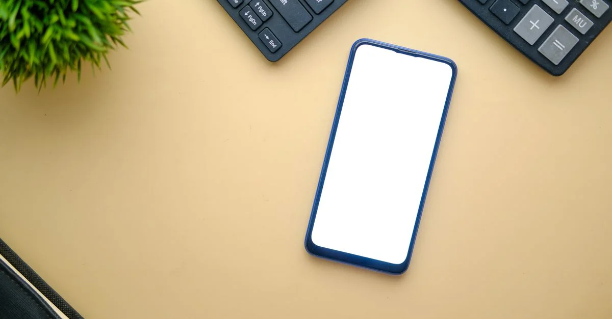 Une vue de dessus minimaliste d'un smartphone sur un bureau avec un clavier et une plante, parfait pour des maquettes.
