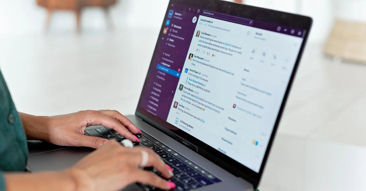 Femme tapant sur un ordinateur portable avec une application de messagerie dans un cadre domestique, gros plan sur les mains.