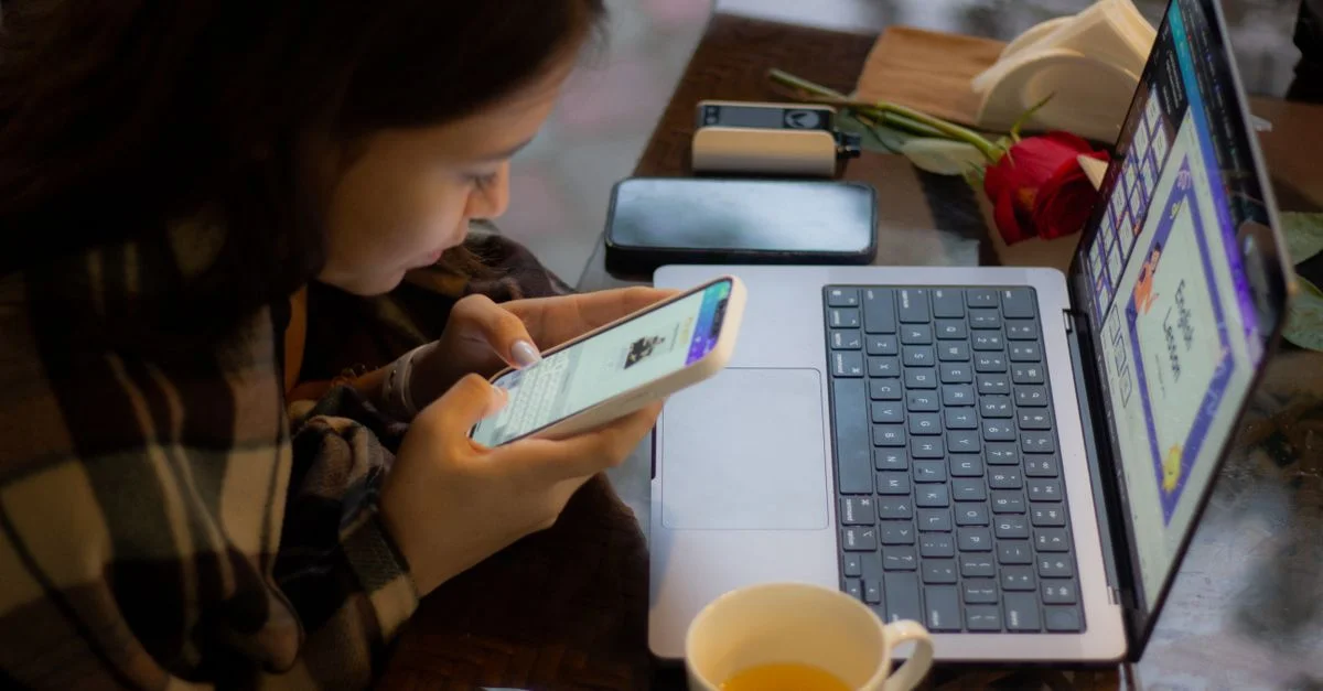 Une femme utilise son téléphone portable et son ordinateur portable simultanément à une table. Parfait pour des images de style de vie ou de technologie.