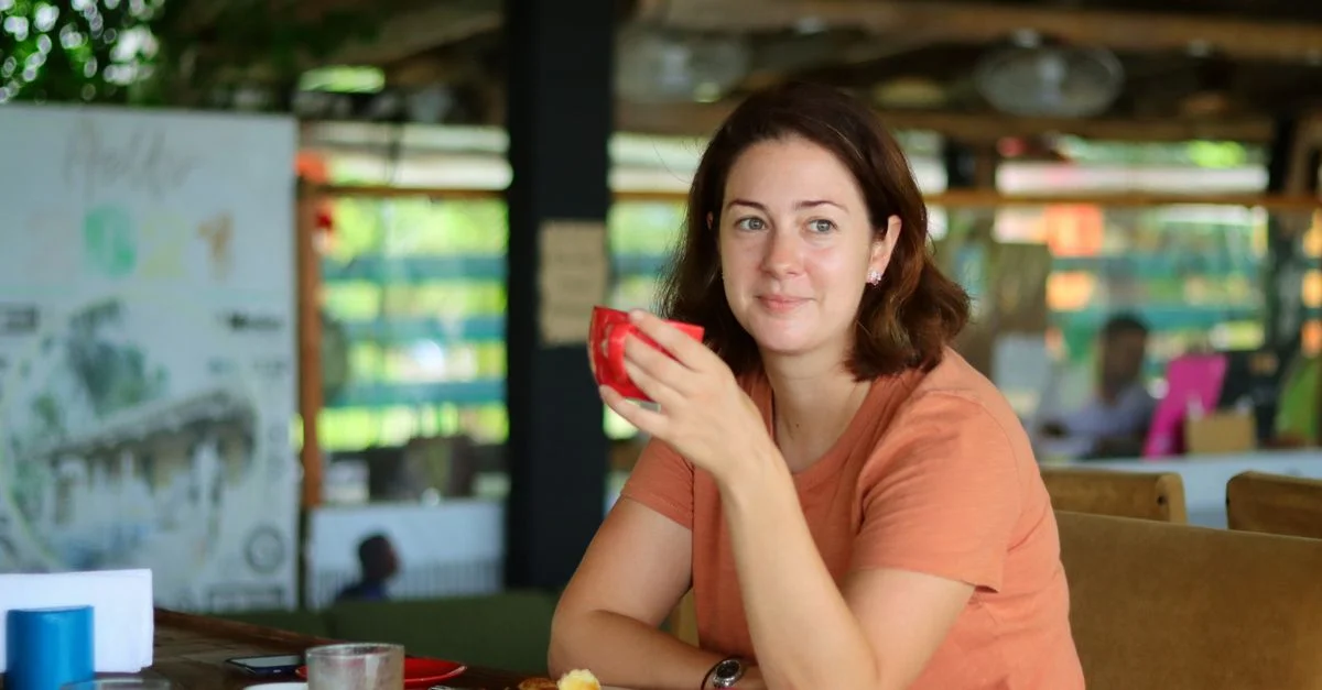 Une femme aux cheveux bruns déguste une boisson dans un café intérieur confortable, dégagent une atmosphère de détente et de confort.