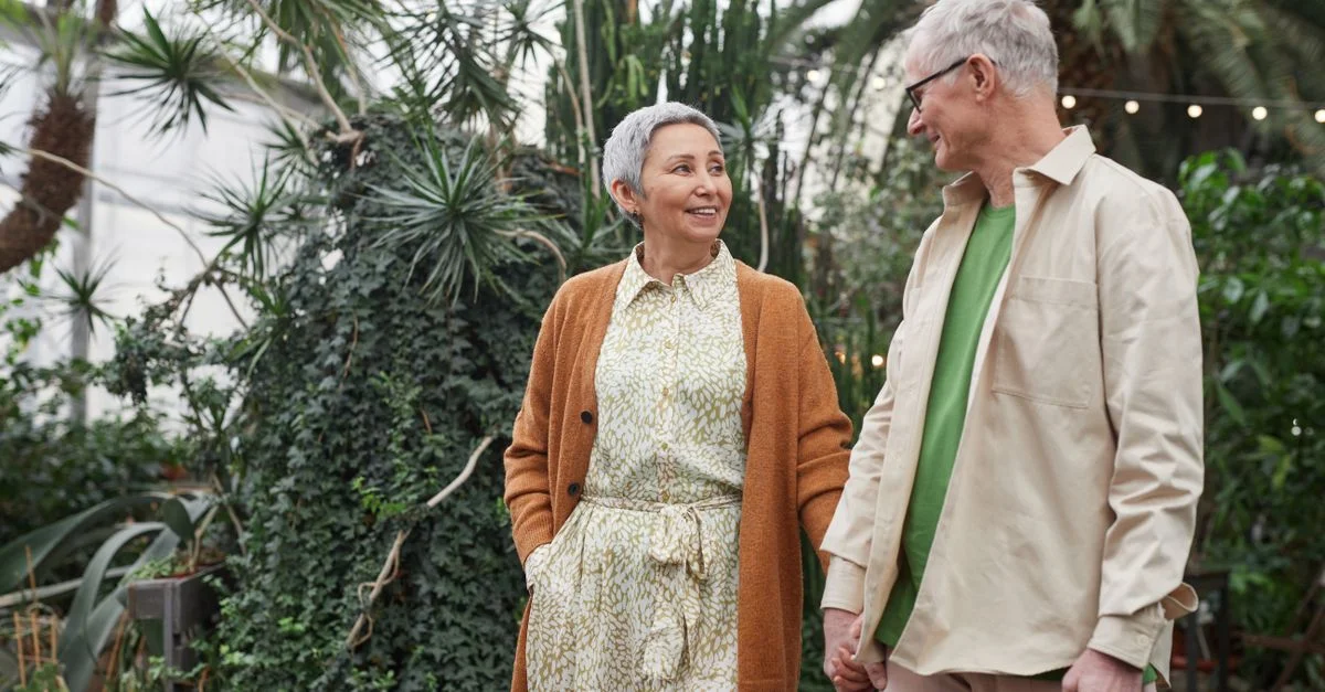 Couple senior profitant d'un rendez-vous dans un jardin botanique luxuriant, partageant des sourires et se tenant par la main.