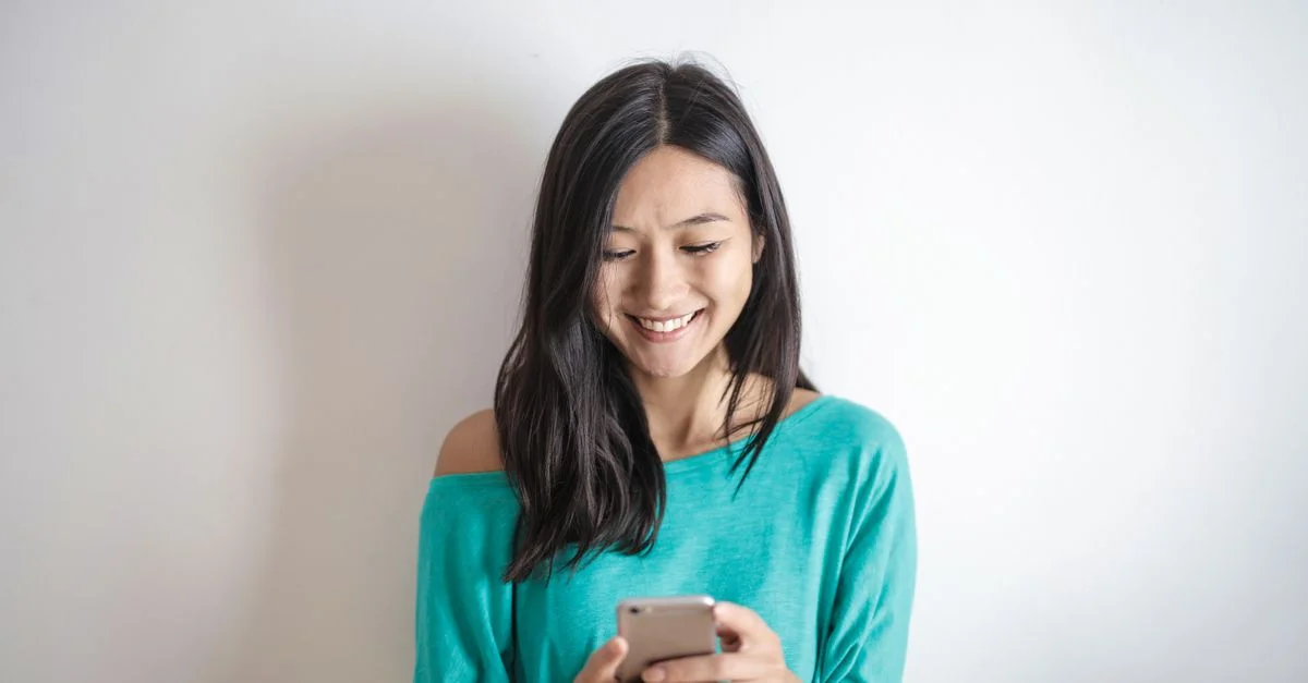 Une femme heureuse en haut vert souriante en utilisant son smartphone à l'intérieur.