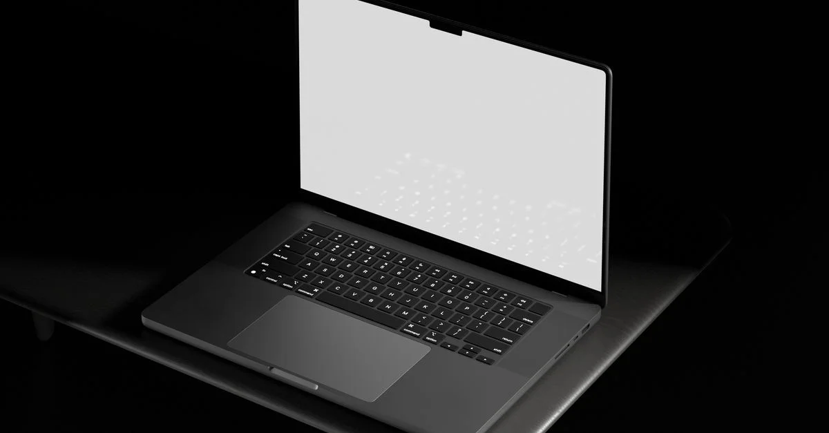 Ordinateur portable ouvert avec un écran blanc vide sur une table dans un cadre sombre, adapté pour des maquettes et des designs.