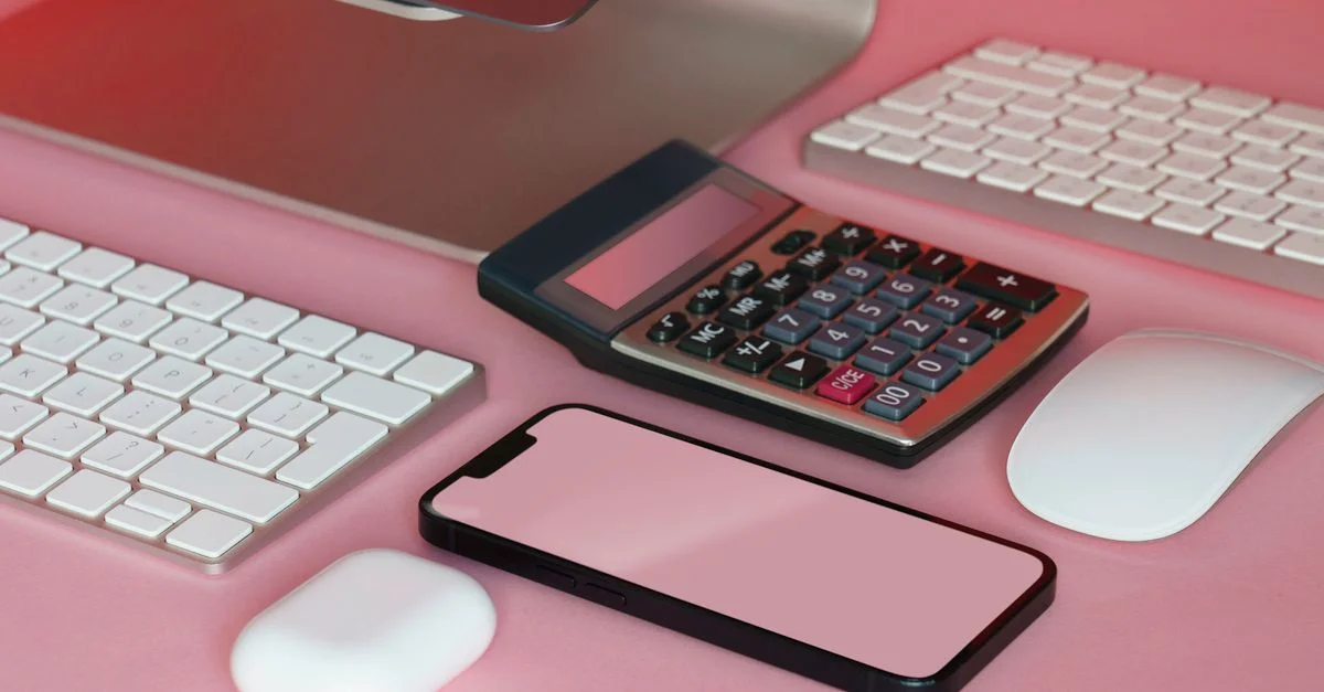 Un ensemble élégant de gadgets de bureau sur une surface rose, incluant un smartphone et une calculatrice.