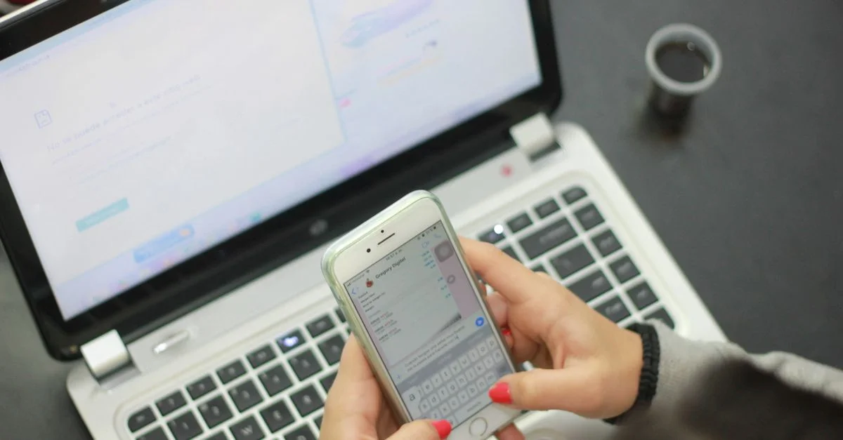 Gros plan d'une femme envoyant un texto sur un smartphone pendant qu'un ordinateur portable est ouvert, indiquant le multitâche.