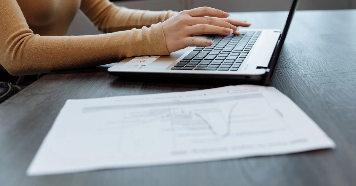 Gros plan sur les mains d'une personne tapant sur un ordinateur portable sur un bureau avec des documents. Idéal pour des thèmes de bureau, de travail et de technologie.