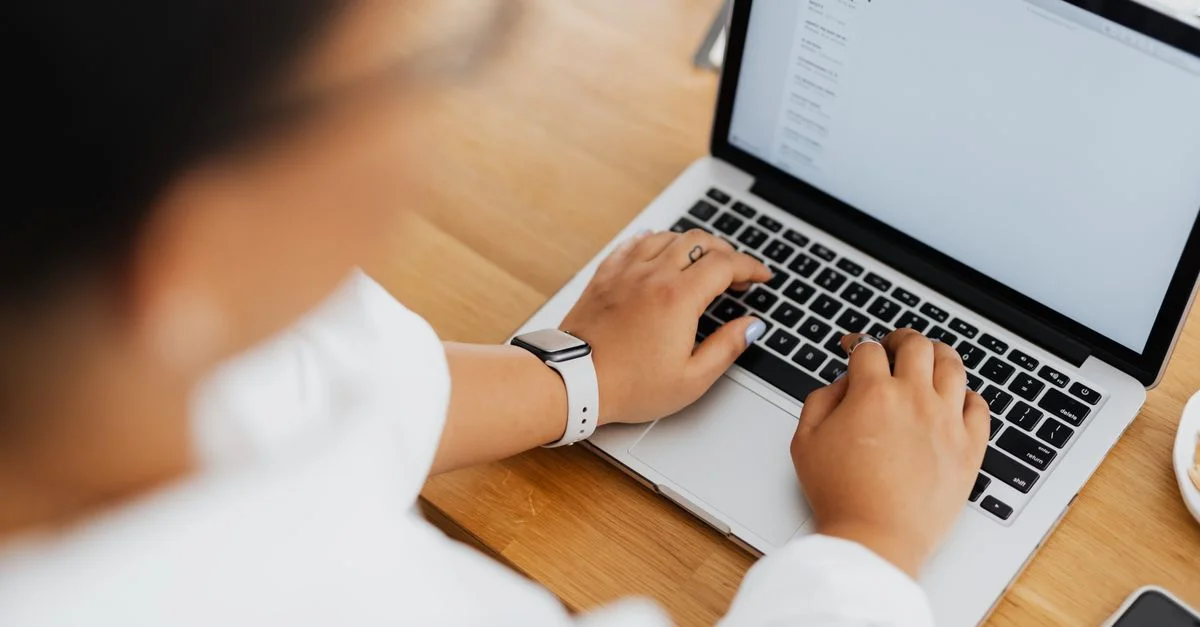 Vue en plongée d'une personne tapant sur un ordinateur portable, centrée sur les mains et le clavier.