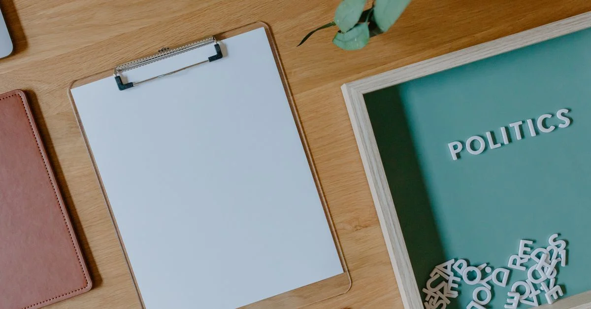 Vue de dessus d'un clipboard blanc, des lettres éparpillées et un thème politique sur un bureau en bois.